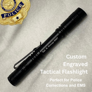May include: Black tactical flashlight with a pocket clip, engraved with "Sgt. N. George #267." The image also shows a police badge. Text on the image reads "Custom Engraved Tactical Flashlight."