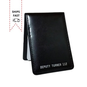 May include: Black leather notebook with the text "DEPUTY TURNER 112" embossed in silver lettering.
