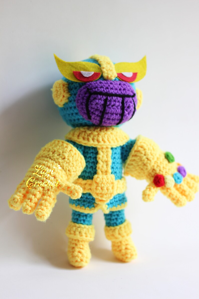 Puede incluir: Un juguete de Thanos tejido a crochet con una cara morada, guantes amarillos y un cuerpo azul. El juguete lleva un casco amarillo con ojos rojos y blancos. El juguete sostiene el Guantelete del Infinito en su mano derecha.