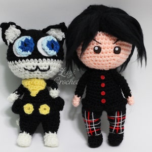 May include: Crocheted plush toys of a black cat with blue eyes and a human character with black hair and red buttons. The cat is wearing a yellow collar and black trousers. The human character is wearing a black shirt and red and white checked trousers.