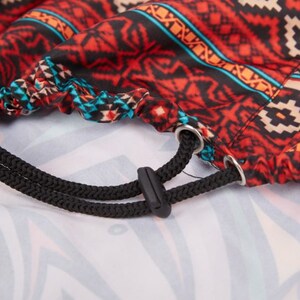 May include: A drawstring bag with a red, black, and blue geometric pattern. The bag has a black drawstring with a toggle.