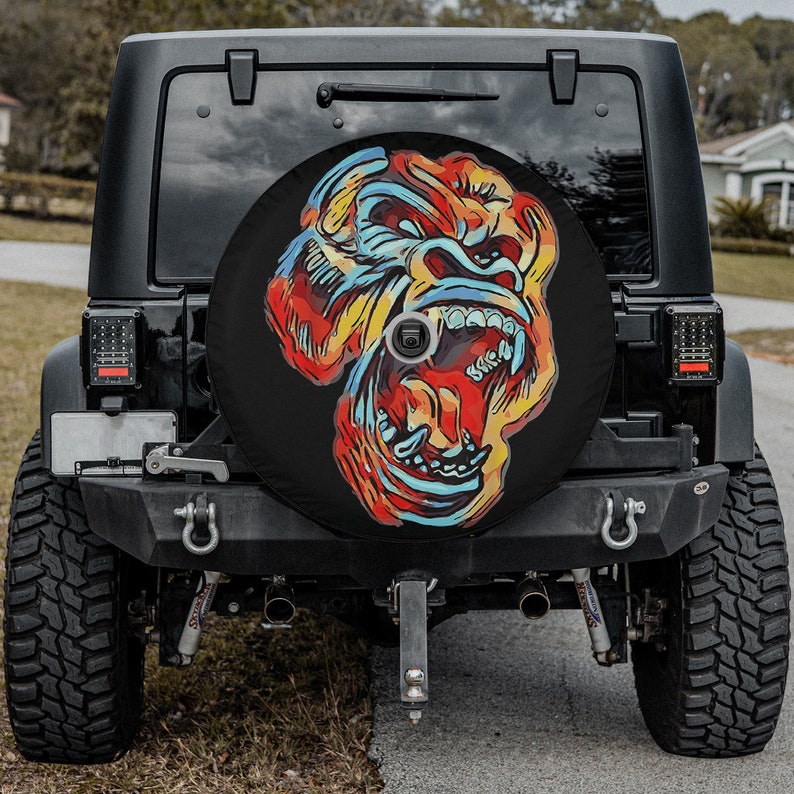May include: A black Jeep with a spare tire cover featuring a colorful, graphic illustration of a gorilla's face with an open mouth and sharp teeth.
