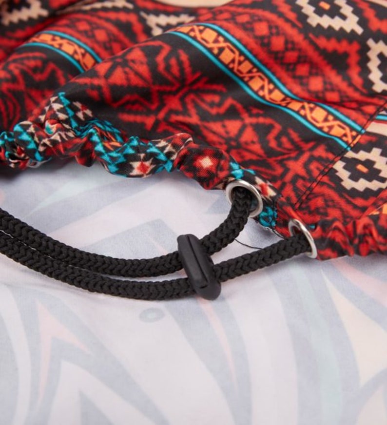 May include: A drawstring bag with a red, black, and blue geometric pattern. The bag has a black drawstring with a toggle.
