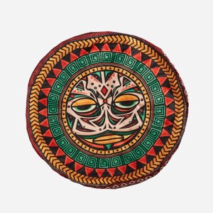 May include: A round, colorful cushion with a tribal design. The center of the cushion features a stylized face with geometric patterns in shades of red, green, yellow, and black.