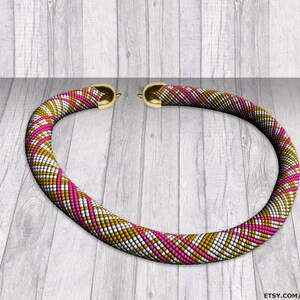 Può includere: Una collana di perline con un motivo geometrico dorato e bianco e accenti rosa. La collana è realizzata con piccole perline e ha una chiusura a moschettone.
