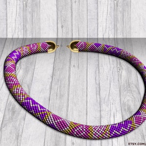 Può includere: Una collana di perline viola, rosa e oro con una chiusura dorata. La collana è su una superficie di legno.