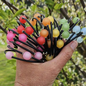 May include: A collection of multiple circular bracelets featuring thin black bands accented with single matte, frosted-finish beads in various colours including pink, red, orange, yellow, green, and blue, separated by small silver-toned metal spacers.