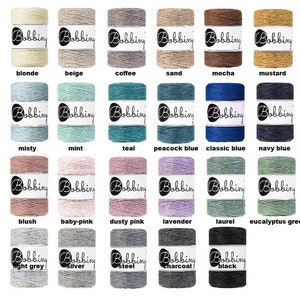 May include: A collection of 24 spools of cotton cord in various colors, including natural, blonde, beige, coffee, sand, mocha, mustard, terracotta, raw denim, misty, mint, teal, peacock blue, classic blue, navy blue, pearl, blush, baby-pink, dusty pink, lavender, laurel, eucalyptus green, avocado, white, light grey, silver, and steel. Each spool has a white label with the word "Bobbing" printed on it.