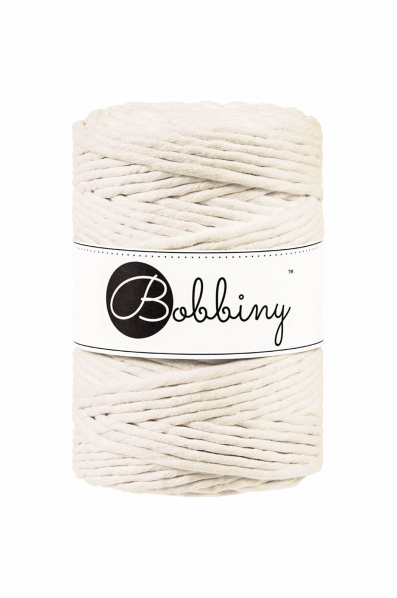 May include: A spool of off-white cotton rope with a white label that says "Bobbiny" in black cursive lettering.