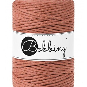 May include: A spool of terracotta colored cotton cord with the label "Bobbiny&trade;" on it.