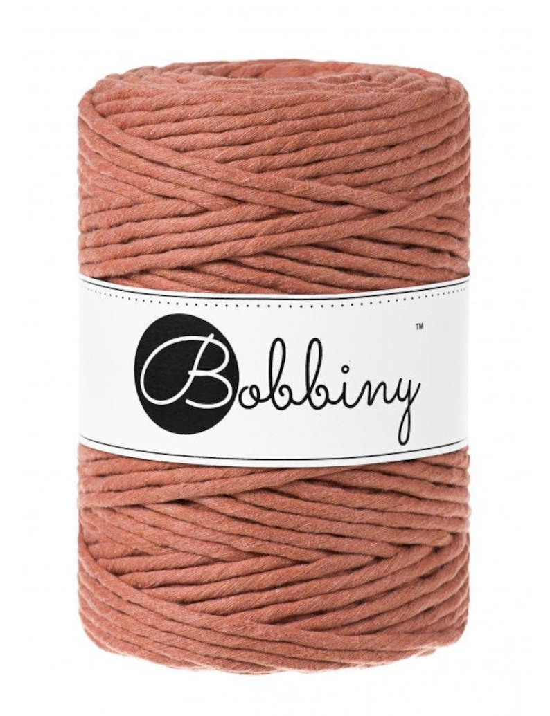 May include: A spool of terracotta colored cotton cord with the label "Bobbiny&trade;" on it.