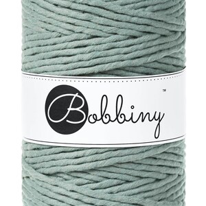 May include: A spool of light green cotton rope with the brand name "Bobbiny" printed on a white label.