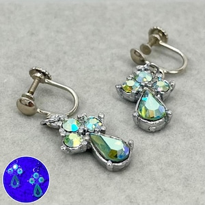 May include: A pair of silver-tone clip-on earrings featuring a teardrop-shaped crystal and smaller crystals clustered together. The crystals are iridescent, displaying shades of green and blue.