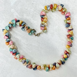 May include: A necklace made of small, colourful seashells, with a gold-coloured clasp. The shells are in shades of pink, blue, yellow, and green. The shells are strung together to form a necklace.