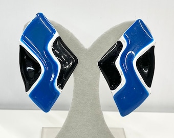 May include: A pair of blue, black, and white geometric clip-on earrings. The earrings are shaped like a diamond and have a modern abstract design.