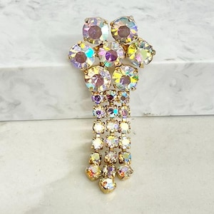 May include: A gold-tone brooch featuring a cluster of round, iridescent aurora borealis rhinestones at the top, with three dangling vertical chains of smaller matching rhinestones extending downward from the central cluster.