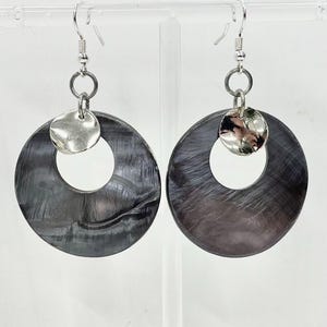 May include: A pair of earrings with large, dark grey, circular pendants with a pearlescent sheen. Each earring has a small, hammered silver disc attached above the larger circle, suspended from a silver hook.