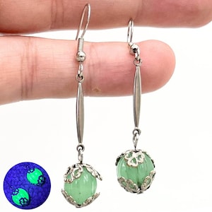 May include: A pair of silver dangle earrings with green jade stone beads. The beads are encased in a silver filigree design. The earrings glow green under a blacklight.
