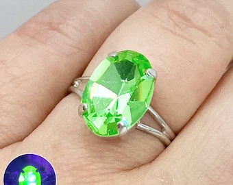 May include: A silver ring with a large, oval-shaped, bright green gemstone. The gemstone glows under a black light.