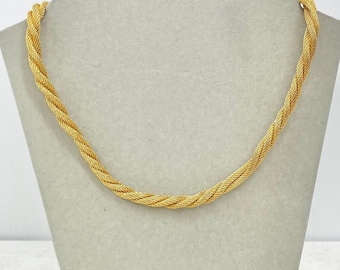 May include: A gold-colored necklace with a braided rope design. The necklace is displayed on a mannequin. The chain is made of small, tightly woven links, creating a textured surface. The necklace is a bright, shiny gold color.