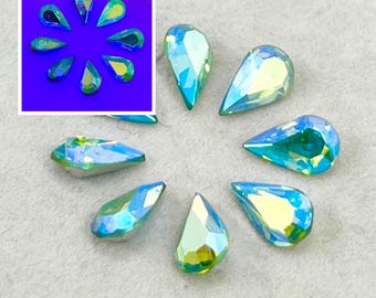Può includere: Una collezione di cristalli a forma di goccia con una finitura iridescente che varia tra tonalità di blu, verde e giallo. La superficie sfaccettata di ogni cristallo riflette la luce, creando un aspetto multicolore sulle pietre.