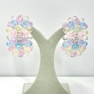 May include: A pair of pastel-colored beaded hoop earrings. The earrings are made of small, round beads in shades of pink, blue, yellow, and clear. The beads are clustered together to form a hoop shape.