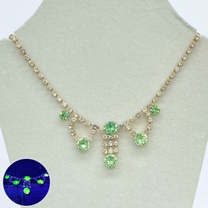 May include: A gold chain necklace with a green rhinestone pendant. The pendant is made up of several smaller rhinestones arranged in a teardrop shape.