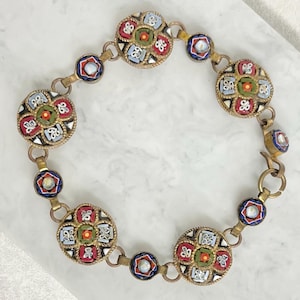 May include: A vintage bracelet with circular mosaic designs in red, green, blue, and white, set in gold-toned metal. The bracelet has a series of round and geometric links, creating an ornate accessory.