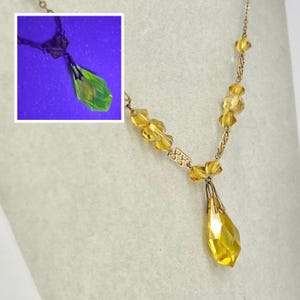 May include: A gold-toned necklace featuring a central faceted yellow crystal pendant and smaller yellow crystal beads along the chain. An inset shows the same pendant glowing bright neon green under ultraviolet light, highlighting its uranium glass composition.
