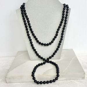 May include: A long, continuous strand of smooth, round, black beads arranged in a double-layered loop. The necklace features uniform, polished black spheres strung together to form a single, unbroken circular design that drapes elegantly.