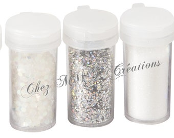 May include: Five small clear plastic jars filled with different types of silver glitter and sequins. The jars are labeled "Chez" and "Créations".