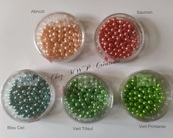 May include: Five small containers of pearl beads in different colors: apricot, salmon, blue, green, and lime green. The containers are labeled with the color names in French.