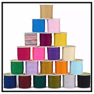 Puede incluir: Una colección de 20 carretes de cordón elástico de colores, dispuestos en forma de pirámide. Los cordones son de varios colores, incluyendo rojo, azul, verde, amarillo, rosa, morado y blanco.