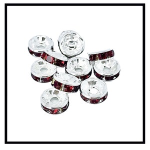 May include: A group of silver-toned bead caps with red rhinestone accents. The bead caps are round and have a hole in the center.