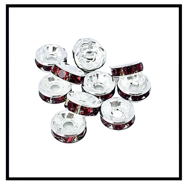 May include: A group of silver-toned bead caps with red rhinestone accents. The bead caps are round and have a hole in the center.