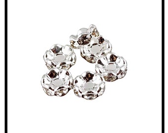 May include: Silver flower-shaped bead caps with clear rhinestones. These caps are used to cover the ends of cords or strings.
