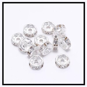 May include: A group of silver-toned metal bead caps with clear rhinestone accents. The bead caps are round with a flat top and a hole in the center.