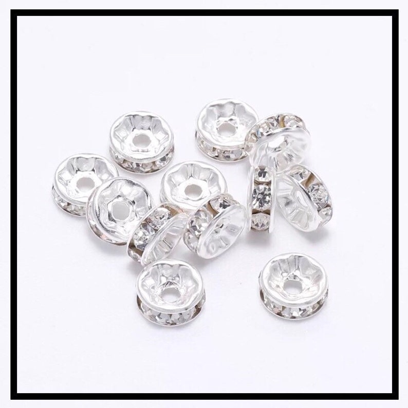 May include: A group of silver-toned metal bead caps with clear rhinestone accents. The bead caps are round with a flat top and a hole in the center.