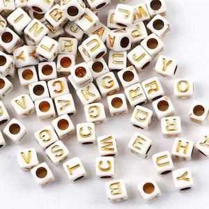 Peut inclure: Perles en plastique blanches en forme de lettres de l'alphabet avec des lettres dorées. Les perles sont en forme de cube et ont un trou au centre.