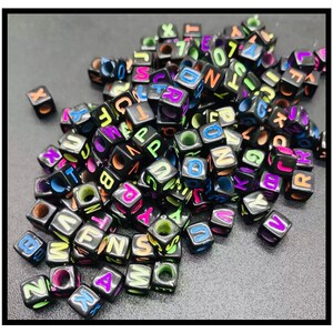 May include: A large pile of black letter beads with colourful neon letters. The beads are cube shaped and have a hole in the centre.
