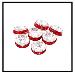 May include: A group of seven silver-toned bead caps with red rhinestone accents. The bead caps are round and have a flat top and bottom.