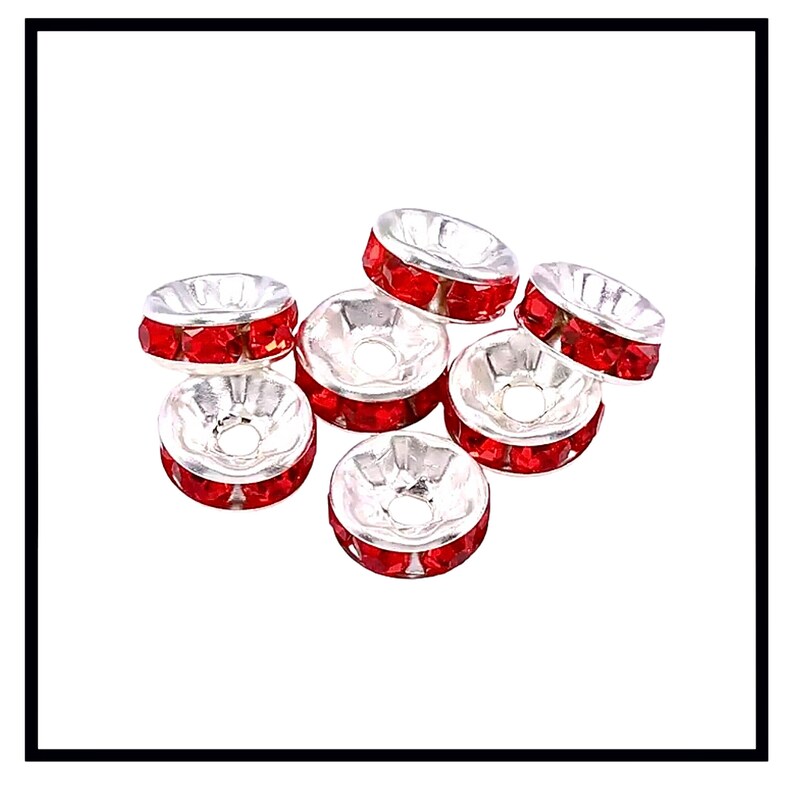 May include: A group of seven silver-toned bead caps with red rhinestone accents. The bead caps are round and have a flat top and bottom.