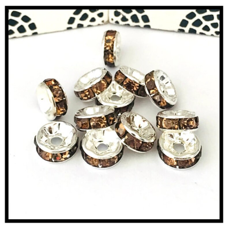 May include: A group of silver-toned bead caps with brown crystal accents. The bead caps are round and have a hole in the center.