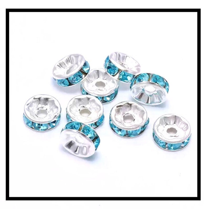 May include: A group of eight silver-toned bead caps with a single row of light blue rhinestones around the edge.