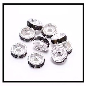 May include: A group of silver-toned bead caps with black crystal accents. The caps are round and have a small hole in the center.