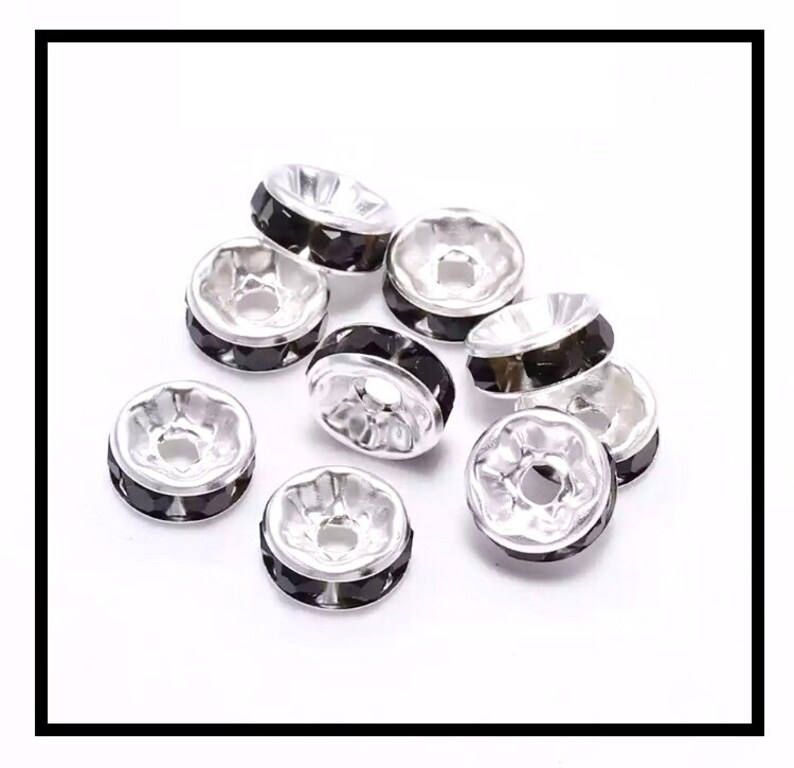 May include: A group of silver-toned bead caps with black crystal accents. The caps are round and have a small hole in the center.