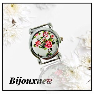 Può includere: Un orologio da polso argentato con quadrante bianco e un motivo floreale con rose rosa. L'orologio ha un cinturino argentato.