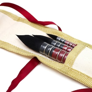 May include: A set of four black and red paint brushes in a beige canvas carrying case with a red ribbon handle.