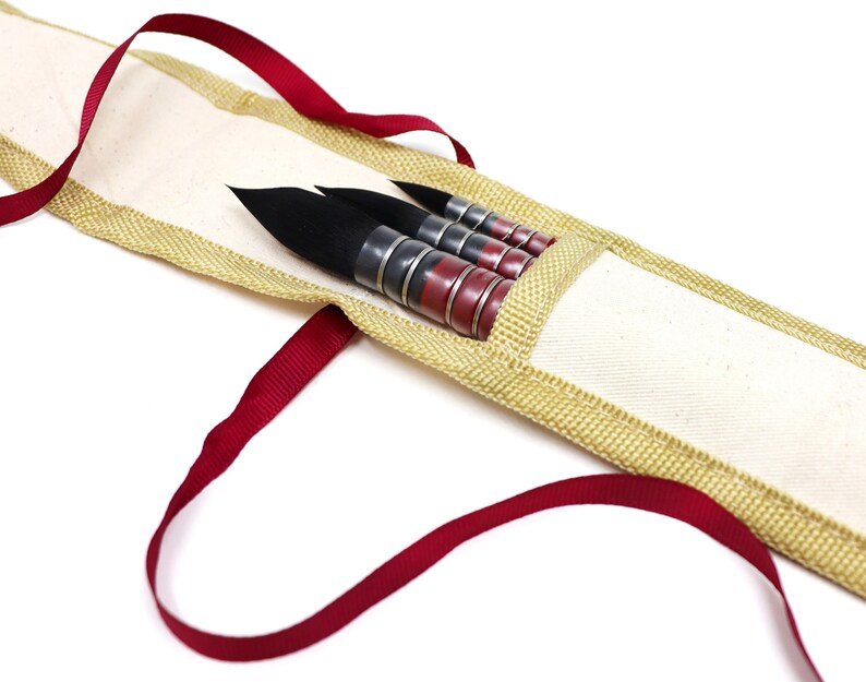 May include: A set of four black and red paint brushes in a beige canvas carrying case with a red ribbon handle.