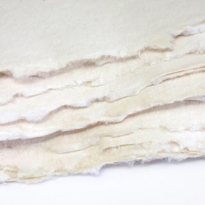 K&ouml;nnte beinhalten: Ein Stapel handgesch&ouml;pften Papiers mit einer rauen, strukturierten Oberfl&auml;che. Das Papier ist cremefarben und hat eine leicht unregelm&auml;&szlig;ige Form.